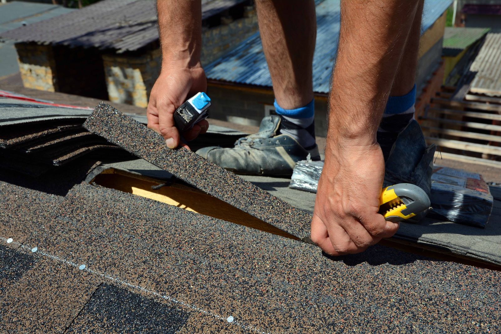 Roofer kneeling on a roof deck fastening architectural shingles by hand